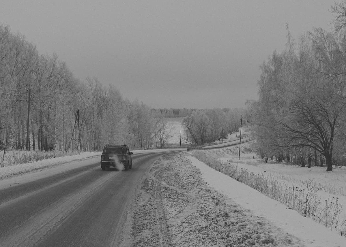 A 2104 Lada is driving through a frozen landscape somewhere near Zaraysk, Moscow Oblast. The snow is very dirty along both edges of the road.